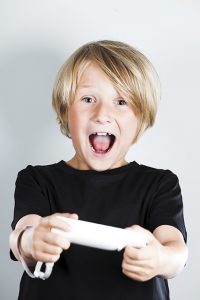 A child holding a video game controller looking excited while playing a game.